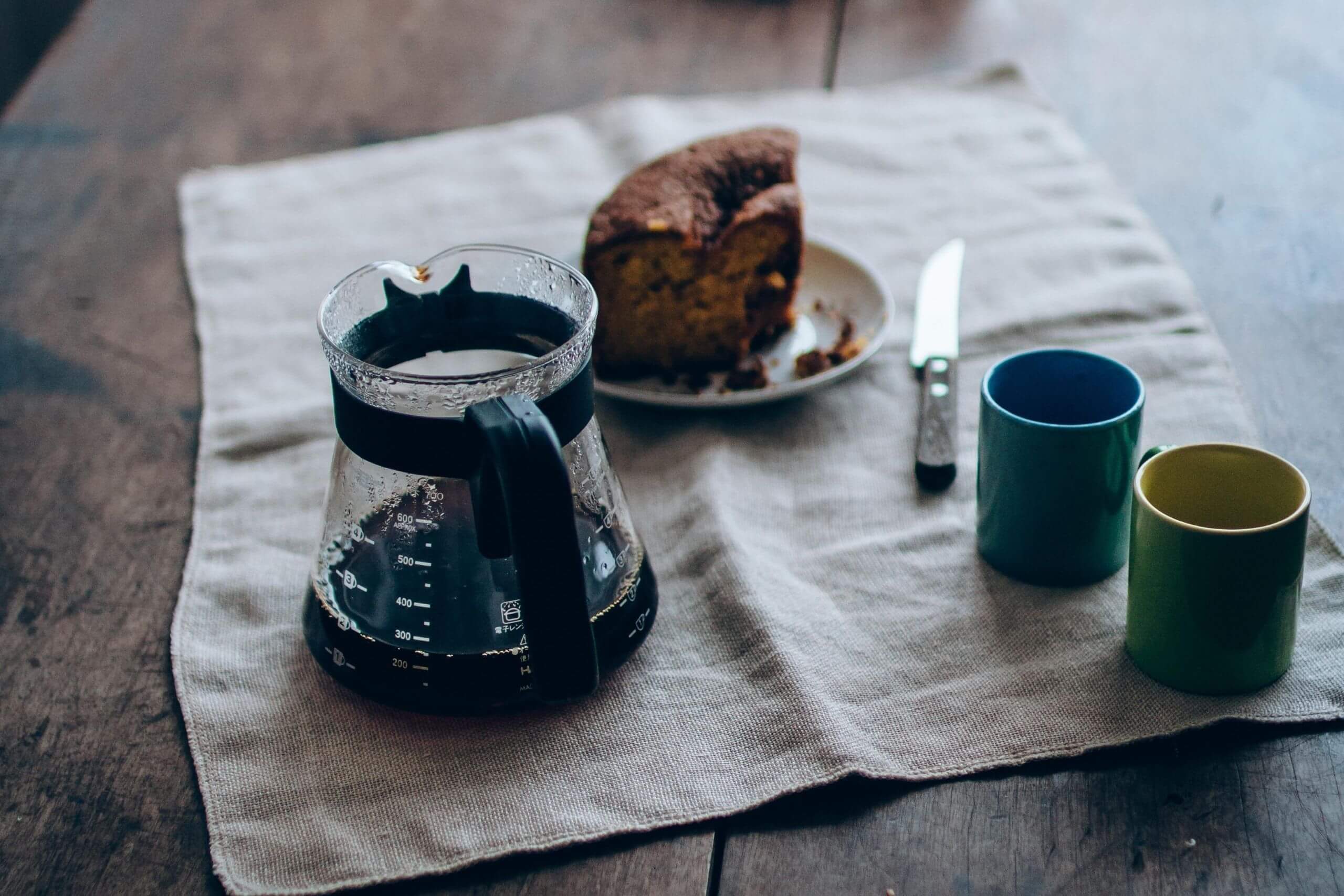 Jarra de vidro com café em cima de mesa com bolo e xícaras