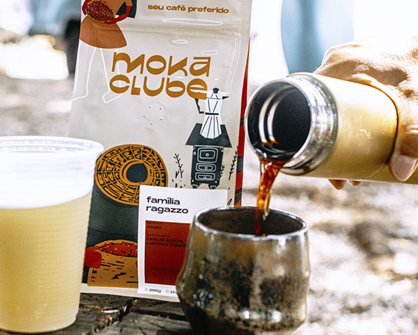Pacote de café família ragazzo a frente um copo de plástico com caldo de cana e ao lado uma garrafa térmica com café e um copo de cerâmica