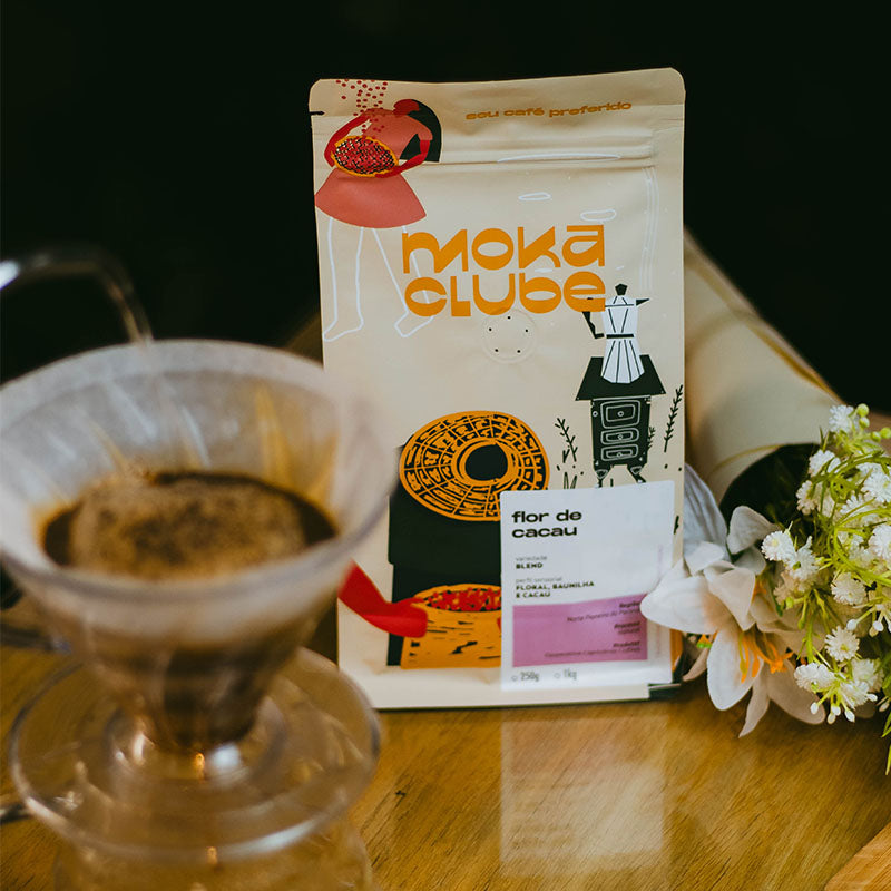 Pacote do café Flor de cacau ao lado um arranjo de flores e um porta filtro V60