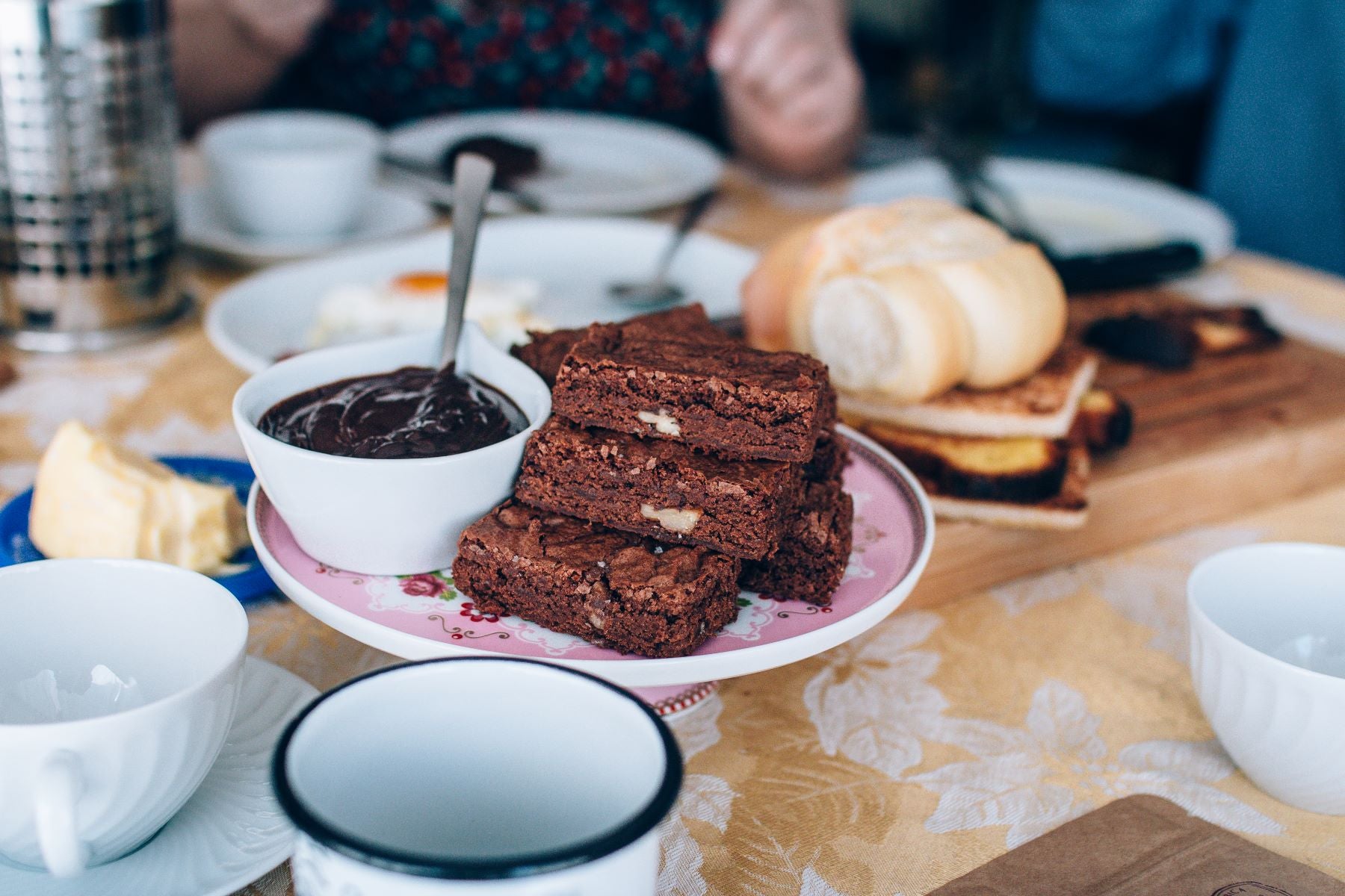 brownie no centro de uma mesa de café da manhã com xícaras e pães