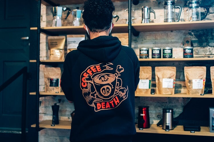 Homem de costas com moletom preto coffee or death olhando para prateleira