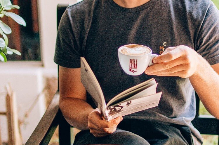 Homem lendo com uma xícara de café na mão