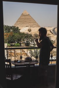 Imagem de um homem tomando café frente a pirâmide do Egito