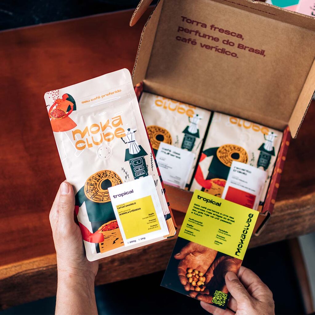 Caixa kit cafés com pessoa segurando um pacote e um cartão postal