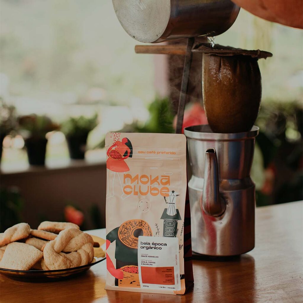 Embalagem café em cima da mesa com prato de bolachas e café sendo preparado em chaleira