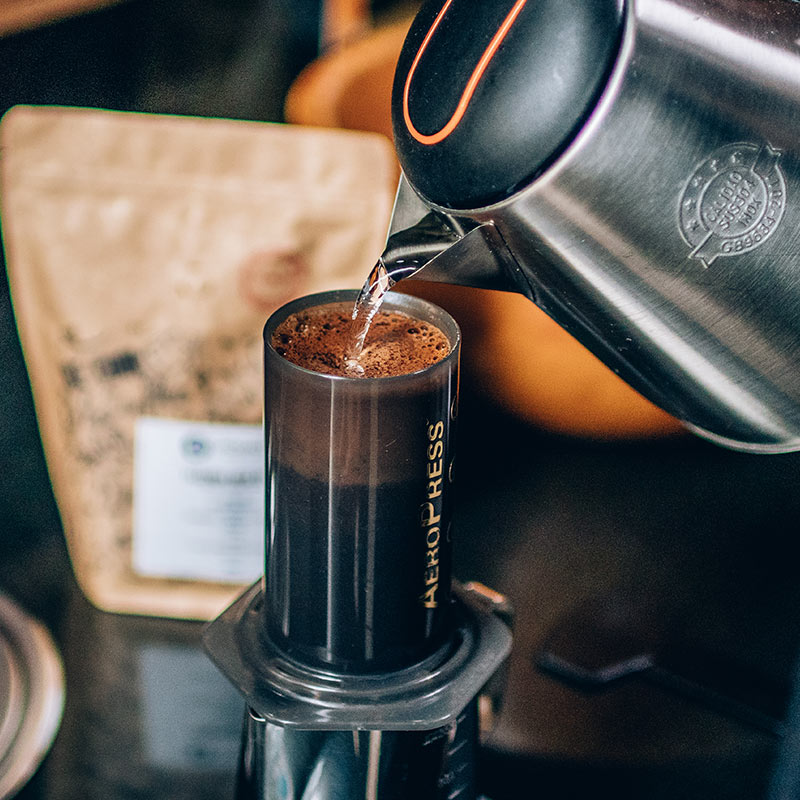 Café sendo preparado na Aeropress com chaleira elétrica e pacote no fundo